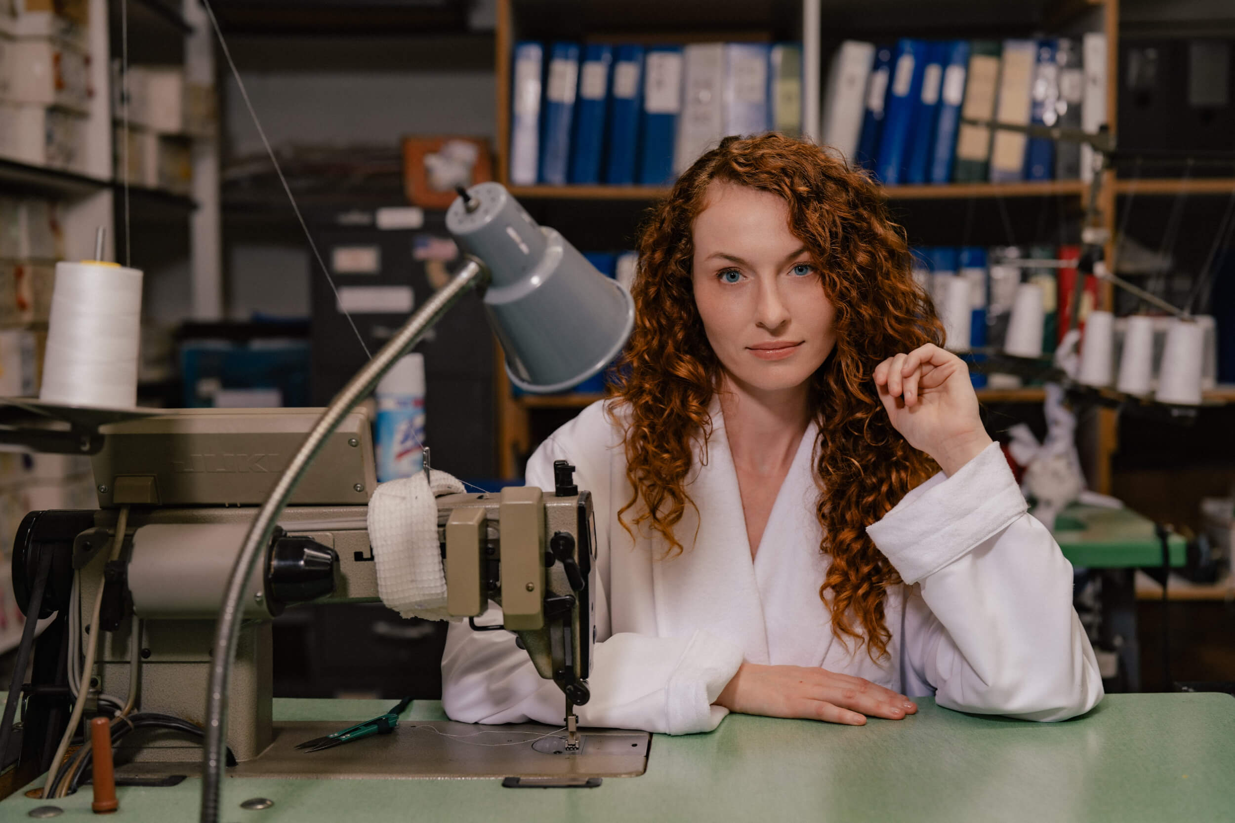 woman sitting at sewing machine wearing white robe